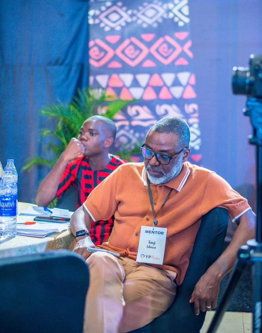 Tunji Idowu seated at an event, wearing a badge that reads Mentor