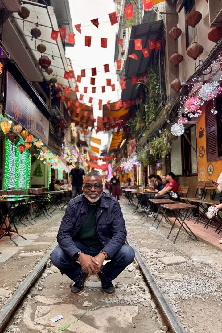 Tunji Idowu crouching on railway tracks in a narrow street lined with cafés, lanterns and hanging flags